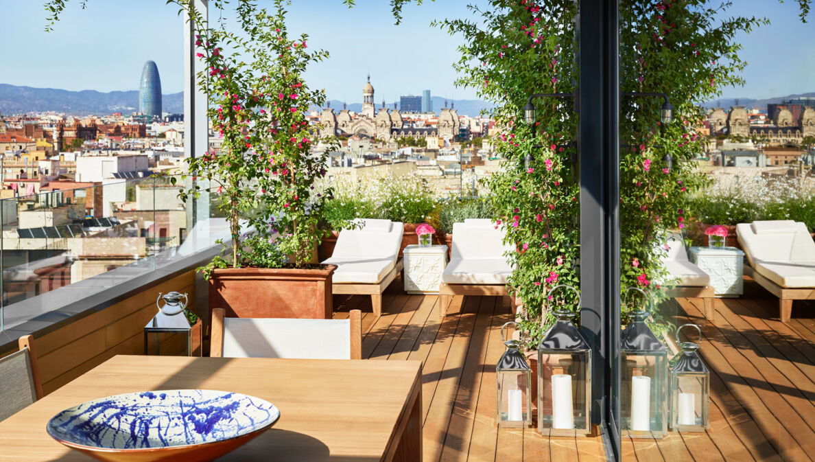 Hotelterrasse mit Liegen vor der Skyline Barcelonas bei Sonnenschein.