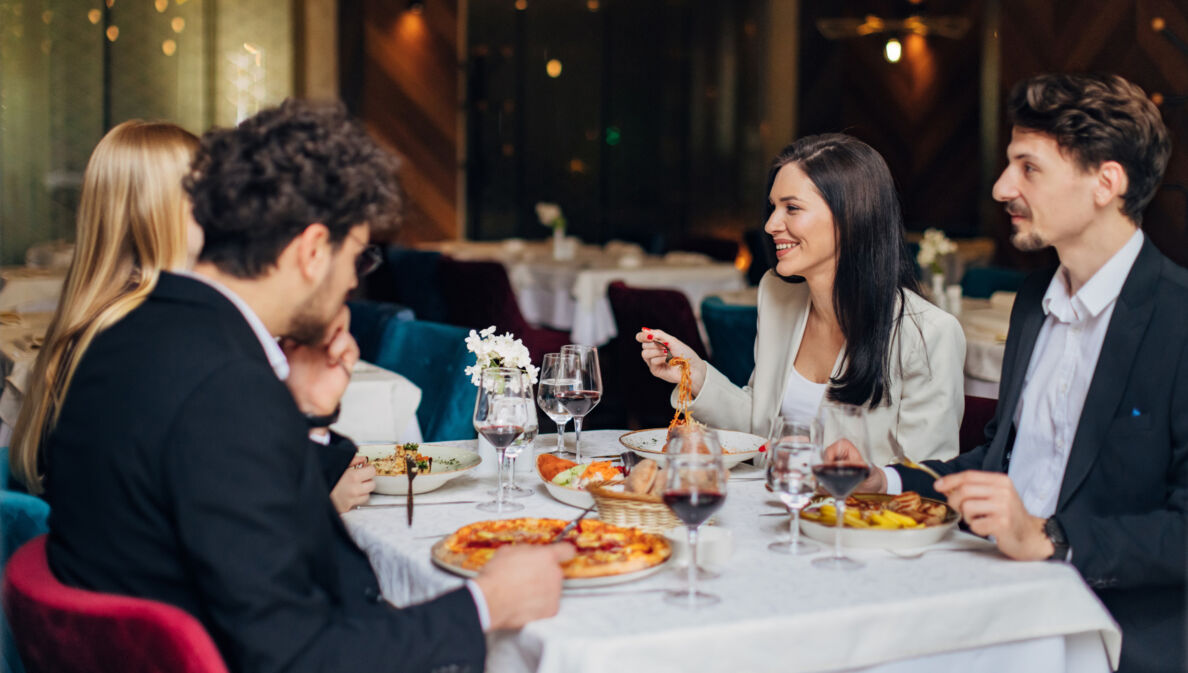 Vier elegant gekleidete Personen sitzen beim Essen an einem Tisch in einem Restaurant.