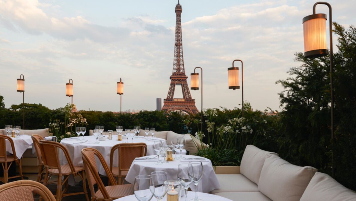 Dachterrasse eines Restaurants mit weiß eingedeckten Tischen vor dem Eiffelturm.