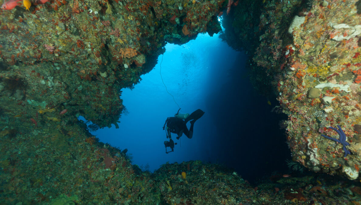 eine Person mit Tauchausrüstung, die aus einer Höhle hinausschwimmt.