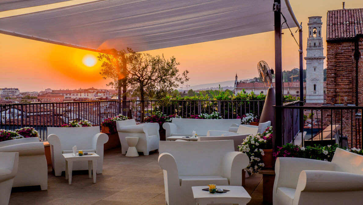 Dachterrasse mit weißen Sitzmöbeln in urbaner, mediterraner Umgebung bei Sonnenuntergang.