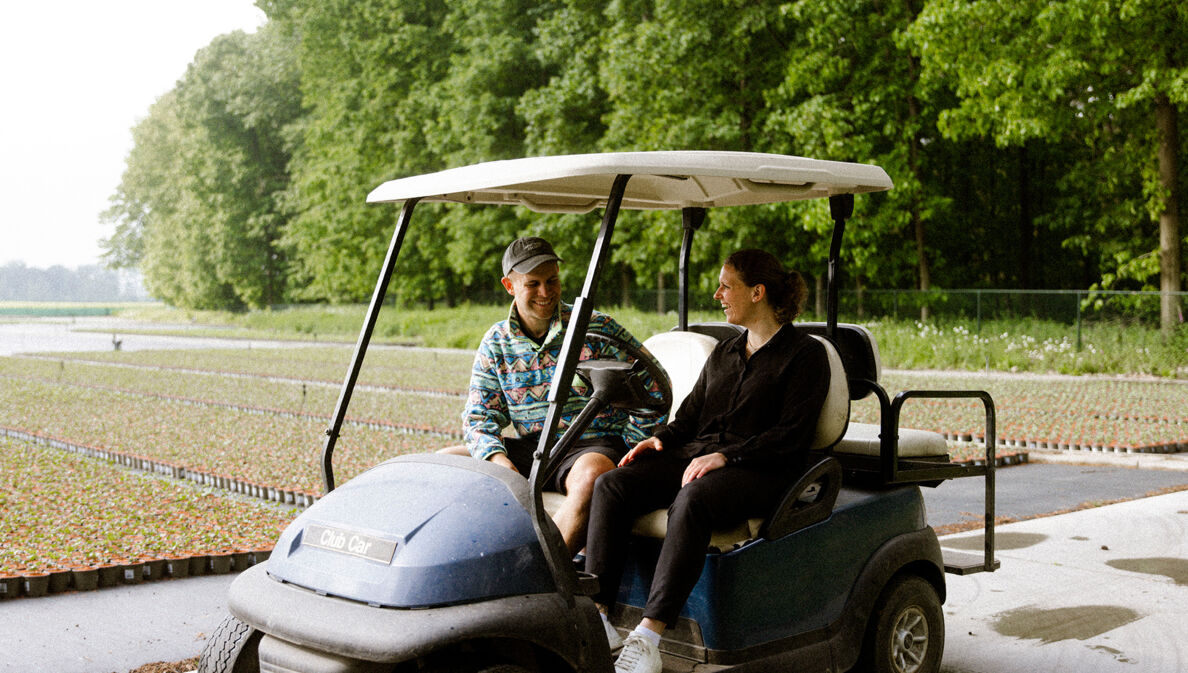 Die Gründerin Antonia Cox sitzt mit Benjamin Diedering in einem Golfplatzfahrzeug und stellt ihm ihr grünes Start-up vor