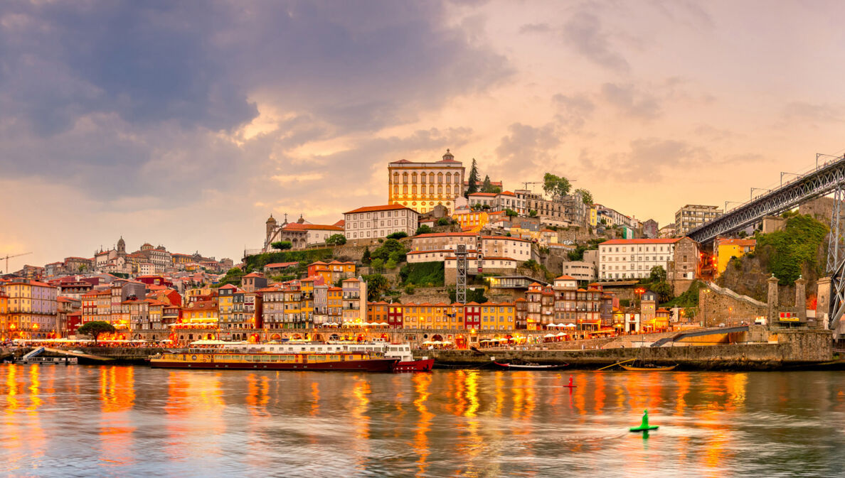 Panoramaaufnahme der Stadt Porto bei Sonnenuntergang mit dem Fluss Duoro im Vordergrund.