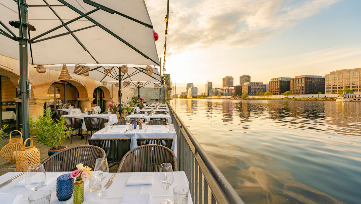 Weiß eingedeckte Tische auf der Terrasse eines eleganten Restaurants am Wasser in Berlin.