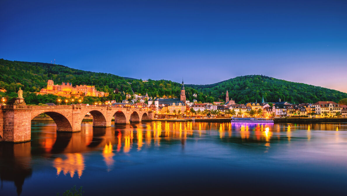 Blick auf die Heidelberger Skyline bei Nacht mit dem Neckar und der Alten Brücke im Vordergrund.