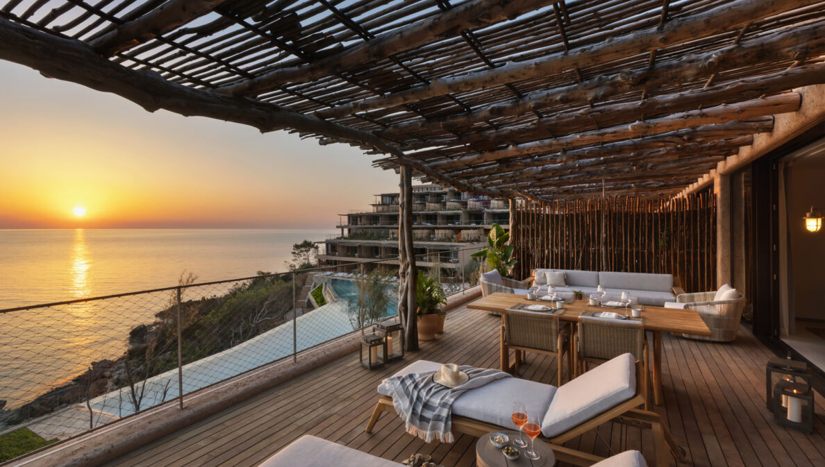 Luxuriöse Hotelterrasse mit Holzpergola am Meer bei Sonnenuntergang.