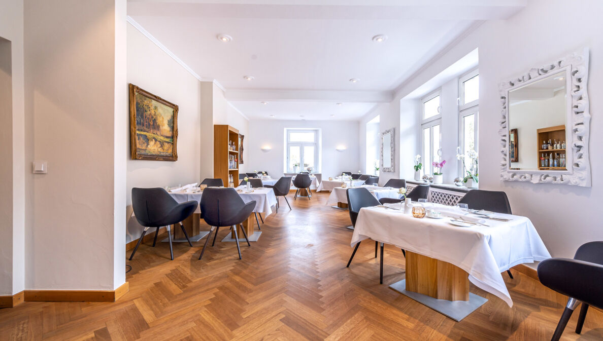 Heller Speisesaal eines gehobenen Restaurants mit Parkett und weiß eingedeckten Tischen.