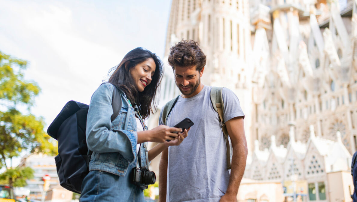 Zwei Personen stehen in Barcelona vor der Sagrada Família und blicken zusammen auf ein Smartphone.