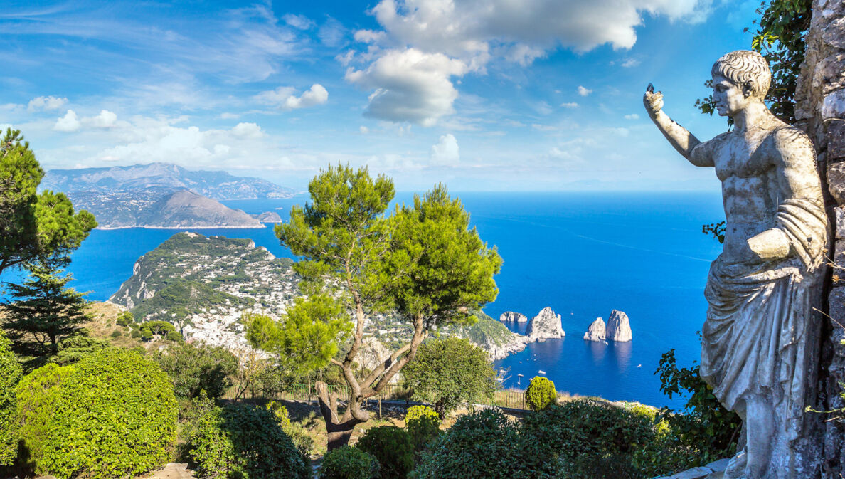 Landschaftspanorama der Insel Capri im blauen Meer, im Vordergrund eine Steinstatue in einem Park.