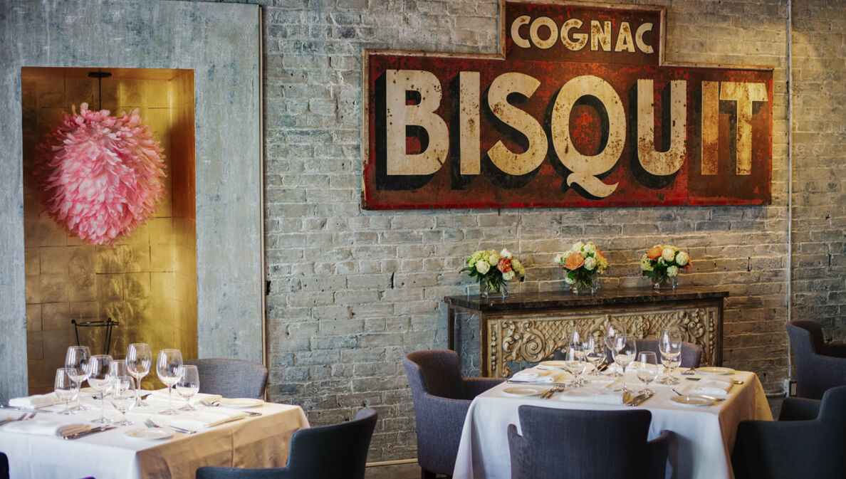 Weiß eingedeckte Restauranttische in einem Raum mit Backsteinwand und antikem Werbeplakat.