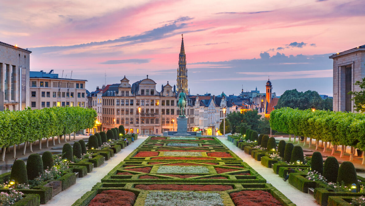 Skyline von Brüssel mit Parkanlage im Vordergrund bei Abenddämmerung unter rosagefärbtem Himmel.