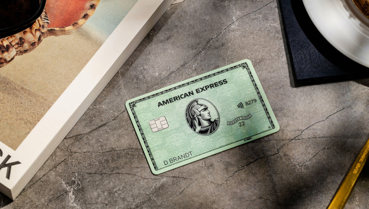 ine grüne American Express Kreditkarte liegt auf einem grauen Marmortisch neben einem Buch.