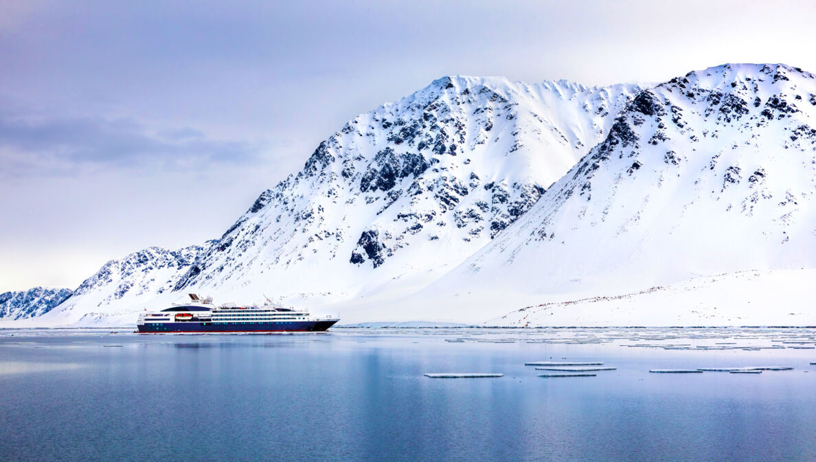 Ein Expeditionsschiff im arktischen Gewässer vor schneebedeckten Bergen.