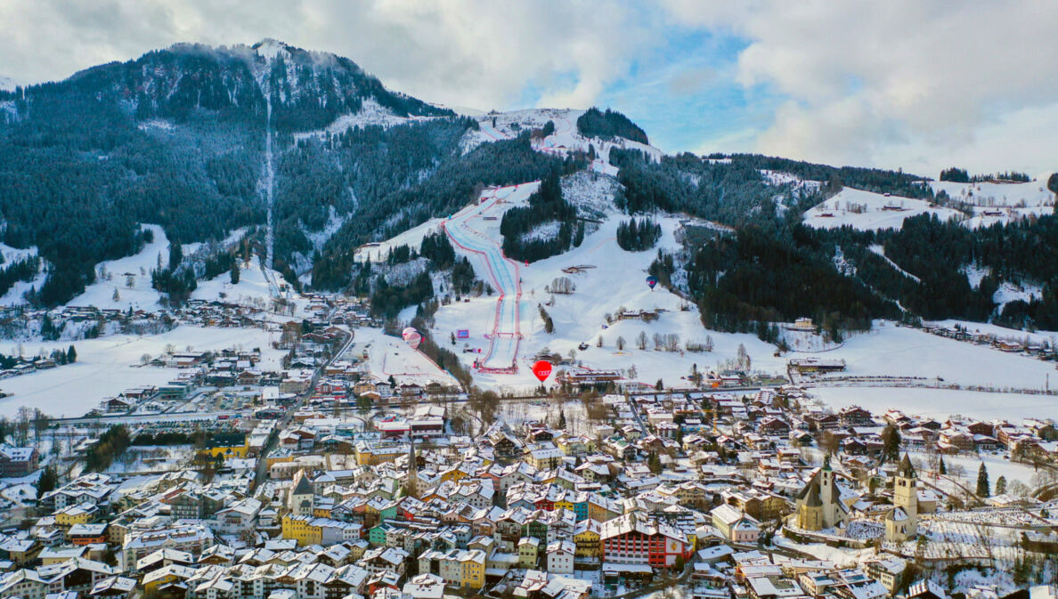 Schneebedecktes Stadtpanorama von Kitzbühel vor Berg mit Skipisten.