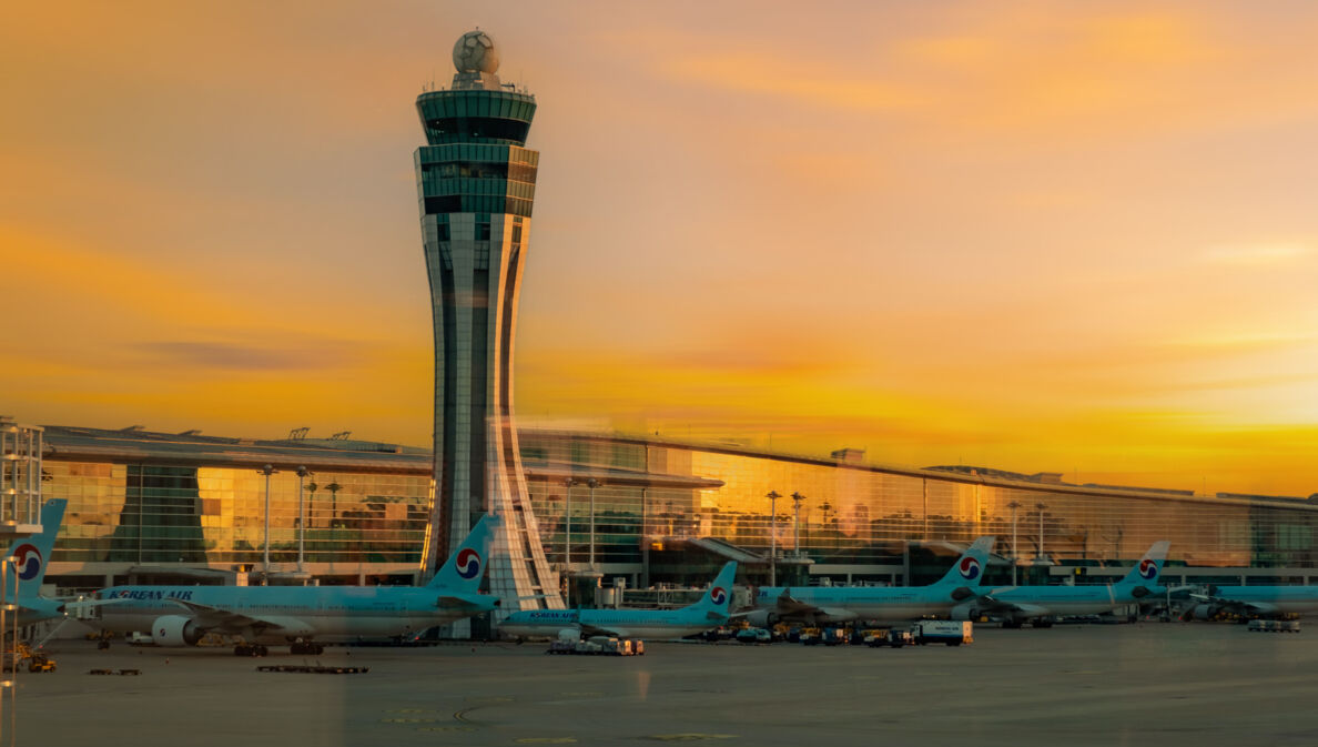 lughafenterminal mit Tower und geparkten Flugzeugen bei Sonnenuntergang.