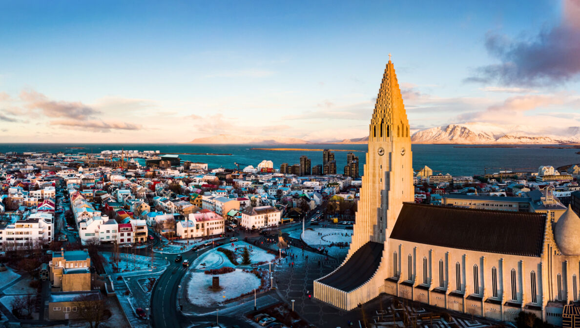 Skyline von Reykjavik mit Pfarrkirche vor Meerespanorama mit schneebedeckten Bergen.