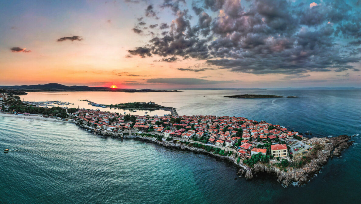 Ortschaft auf einer felsigen Landzunge im Meer unter Wolkenhimmel bei Sonnenuntergang.