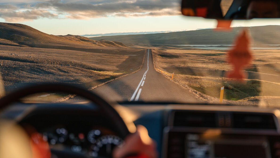 Blick auf eine Landstraße in karger, hügeliger Naturlandschaft durch die Windschutzscheibe eines fahrenden Autos.