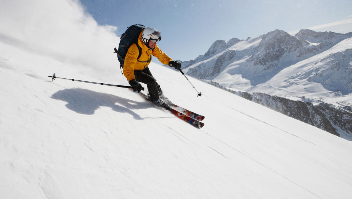 Eine skifahrende Person auf einer Piste vor Bergpanorama.