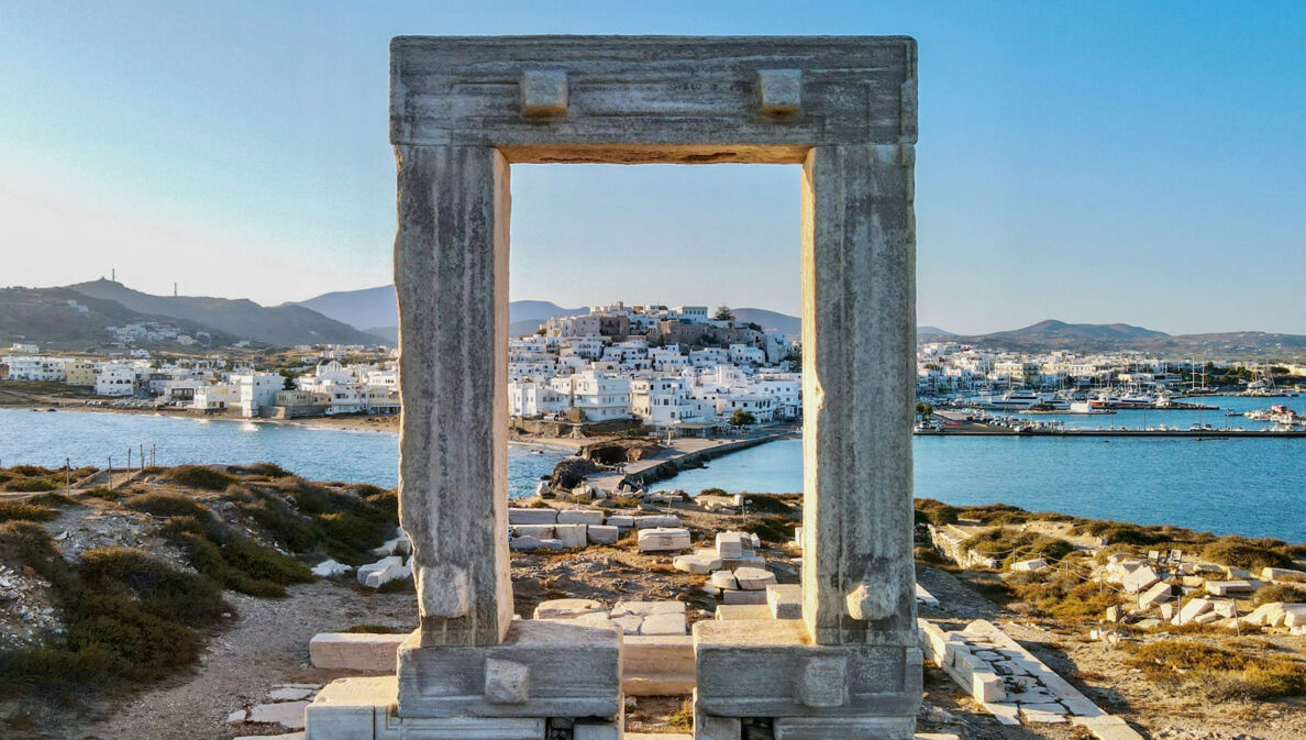 Blick auf die Stadt Naxos auf einer Insel durch ein Steintor in einer antiken Ruinenstätte auf einem Hügel.