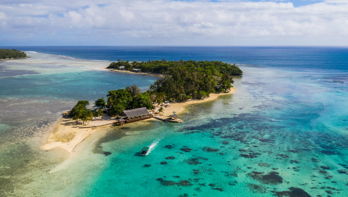 Kleine Insel mit Mangrovenwald und Bootsanleger an einem hellen Sandstrand, umgeben von türkisblauem Meer.