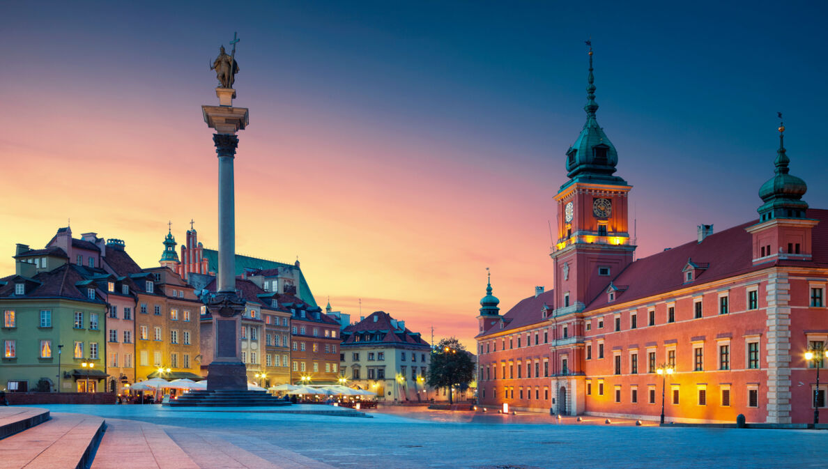 Beleuchteter Marktplatz in der Altstadt von Warschau mit Schlossbau aus rotem Stein und Siegessäule bei Abenddämmerung.