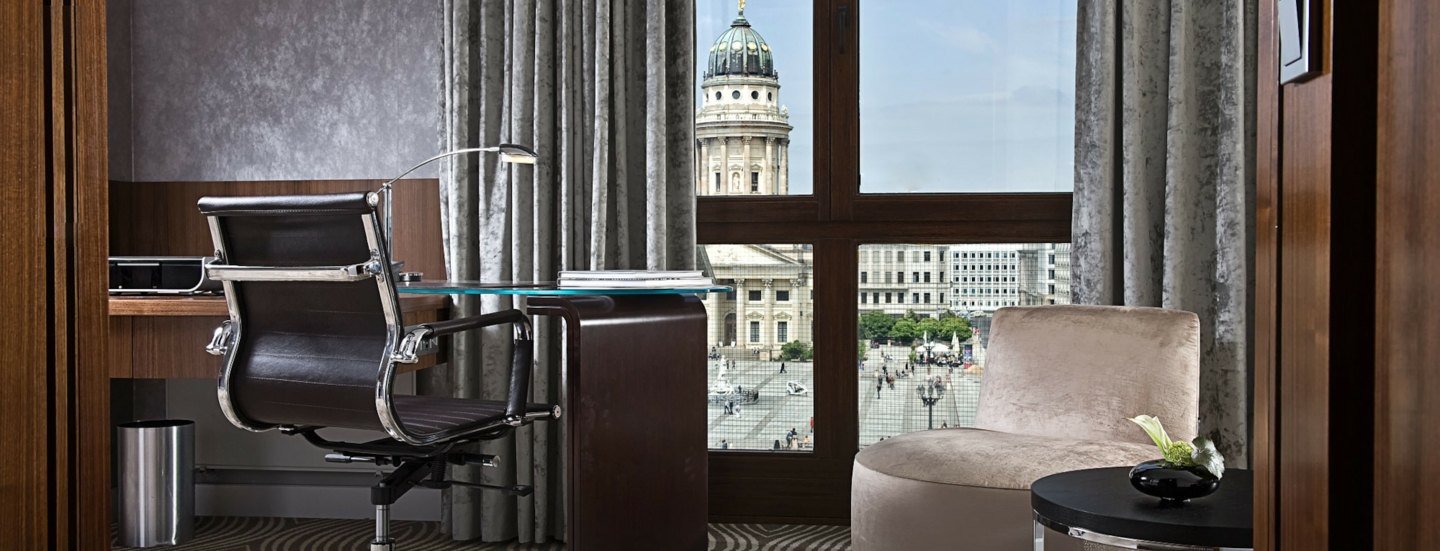 Luxuriöses Hotelzimmer mit Schreibtisch an einem bodentiefen Fenster mit Blick auf den Dom am Gendarmenmarkt in Berlin.