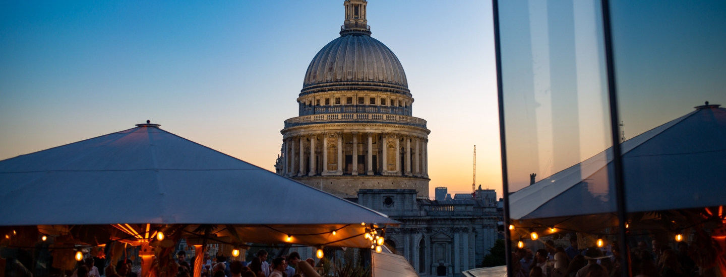 Belebtes Restaurant auf Dachterrasse vor der Kuppel der St Paul’s Kathedrale bei Abenddämmerung.