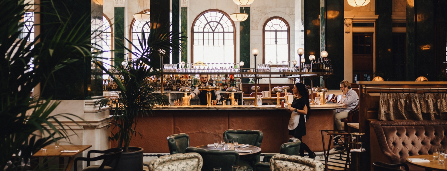 Hotellobby mit grünen Säulen um eine Bar mit Esstischen im 1920er-Jahre-Stil.