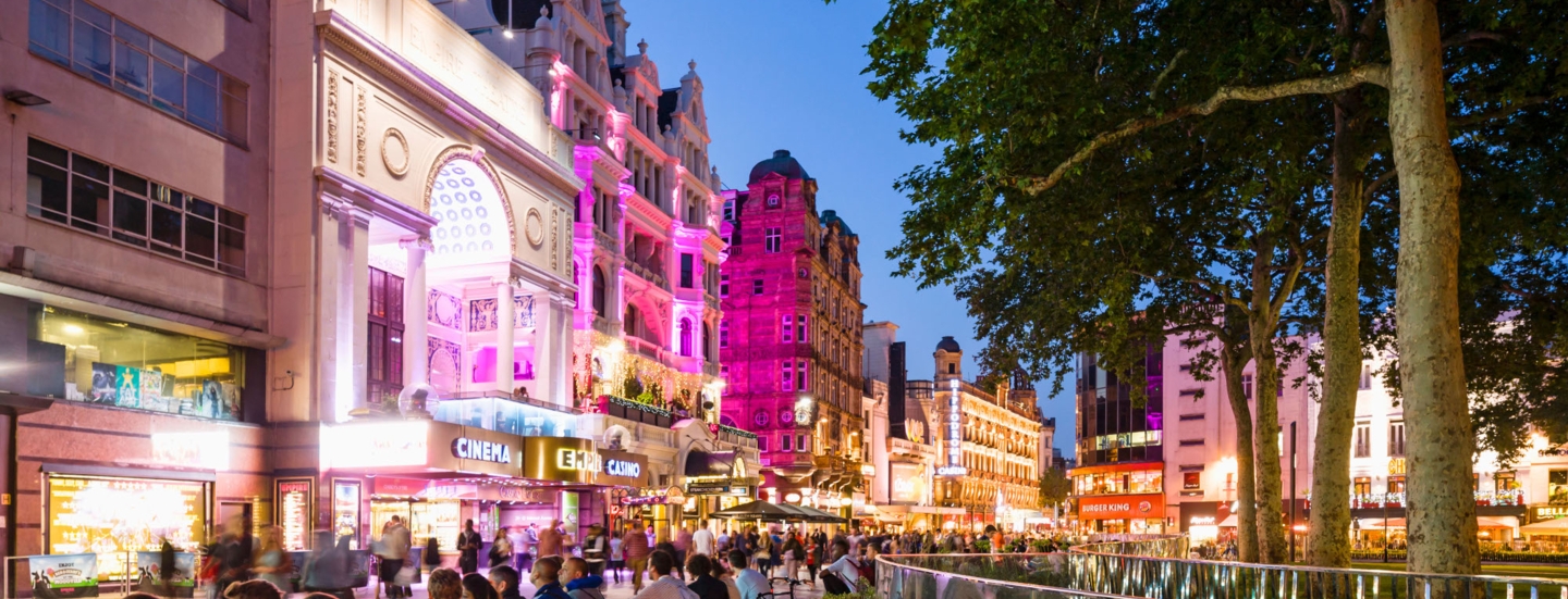 Belebter Leicester Square mit beleuchteter Häuserfassade am Abend.