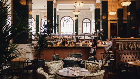 Hotellobby mit grünen Säulen um eine Bar mit Esstischen im 1920er-Jahre-Stil.