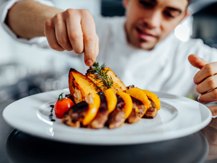 Ein junger Koch dekoriert ein angerichtetes Gourmet-Essen mit Kräutern