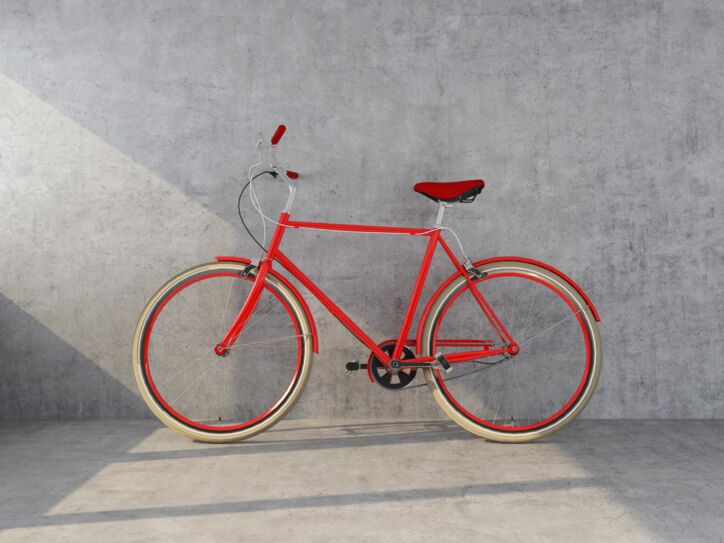 Ein orangefarbenes Designerfahrrad mit Ledersattel vor einer Betonwand