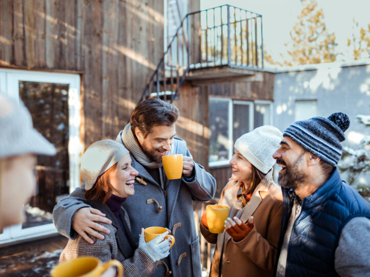 Freunde stehen im Winter vor eine Holzhütte und lachen und reden miteinander