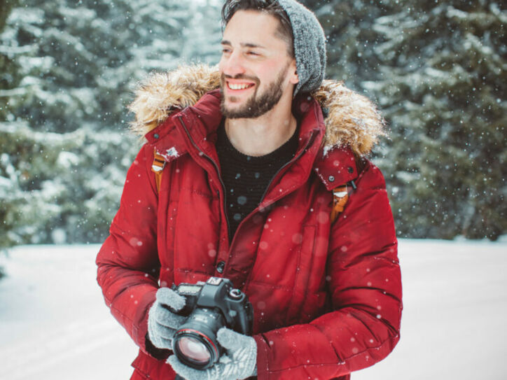 Ein Mann mit Kamera lächelt im Schnee.