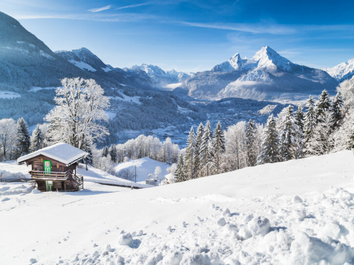 Eine schneebedeckte Berglandschaft, im Vordergrund steht eine kleine Holzhütte