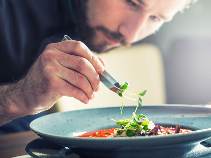 Ein Küchenchef richtet mit der Hand die Tomatensuppe an