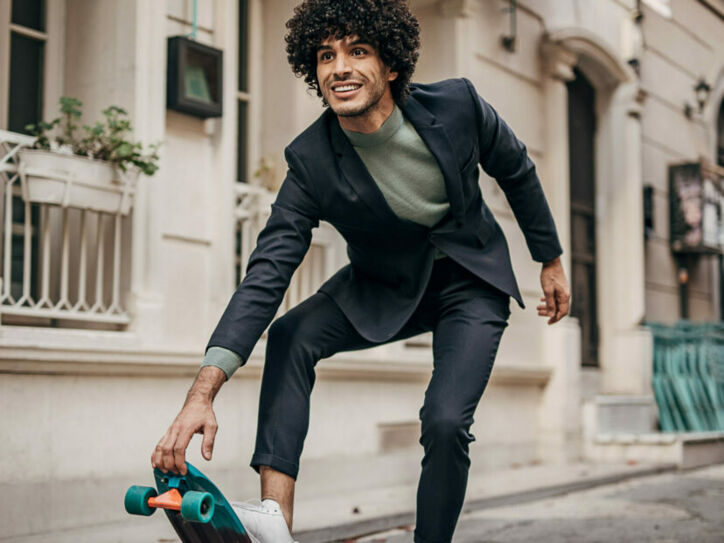 Ein junger Mann mit Anzug und Sneakern auf einem Skateboard in der Stadt