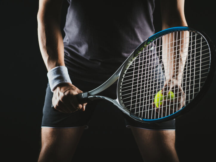 Eine Person hält einen Tennisschläger und Tennisball in der Hand.