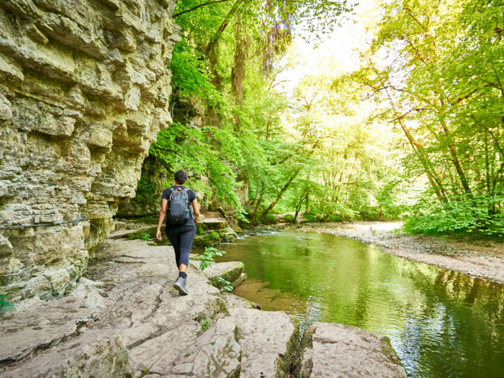 Eine Person mit Rucksack wandert an einem Fluss entlang