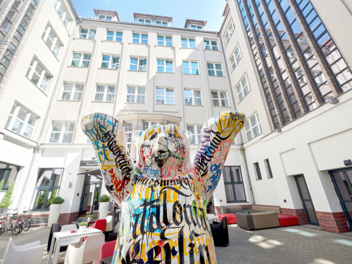 Die Statue eines bunten Berliner Bären steht im Innenhof eines mehrstöckigen weißen Hotels