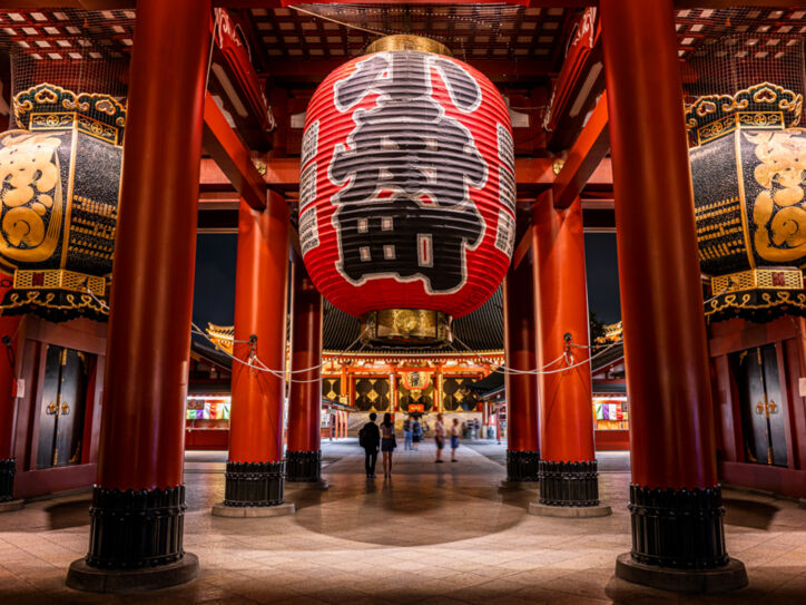 Rote Säulen und überdimensionale Laternen mit japanischen Schriftzügen in einem Tempel