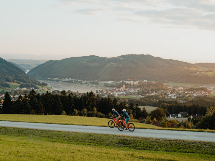 Zwei Radfahrer fahren auf dem Donauradweg mit Blick auf Berge