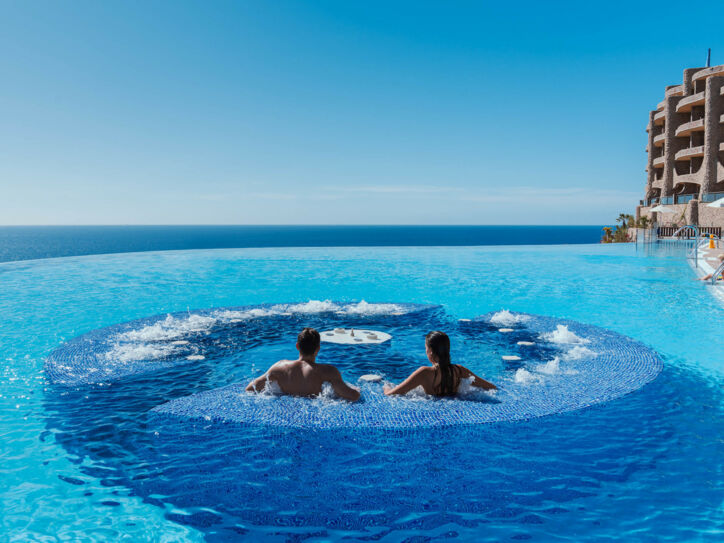 Rückansicht zweier Personen in einem großen Hotelpool mit Jacuzzi am Meer.