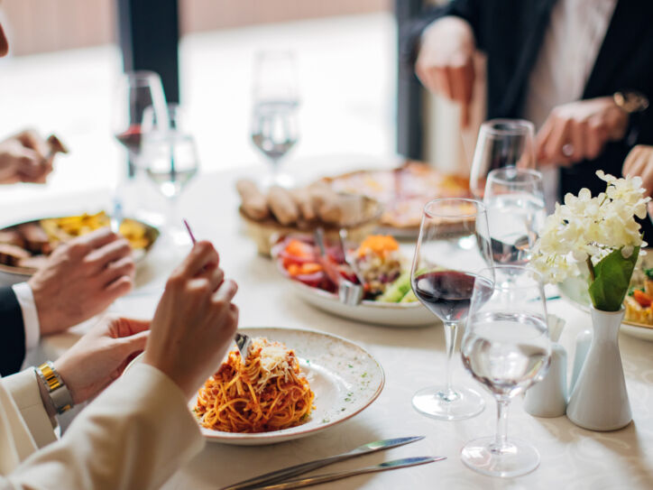 Eine Gruppe Personen an einem weiß eingedeckten Tisch in einem Restaurant mit verschiedenen Gerichten wie beispielsweise Pasta.