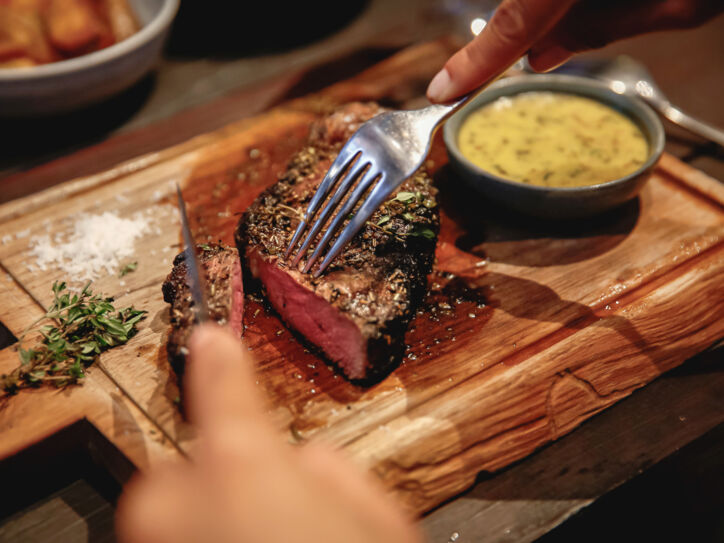 Nahaufnahme eines angeschnittenen Steaks auf einem Holzbrett neben einer Schale mit Soße.