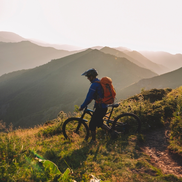 Mountainbiker steht mit seinem Rad auf einem Berg und schaut ins Tal