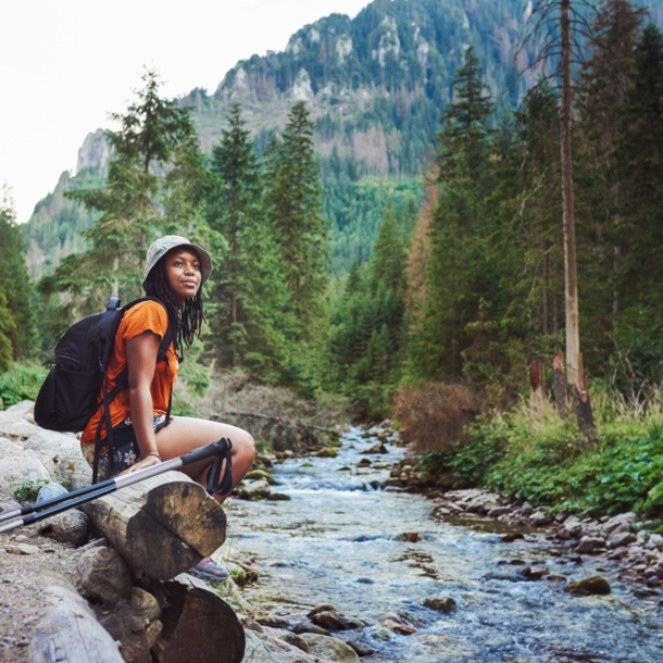 Eine Frau sitzt mit Wanderausrüstung an einem Bach im Wald