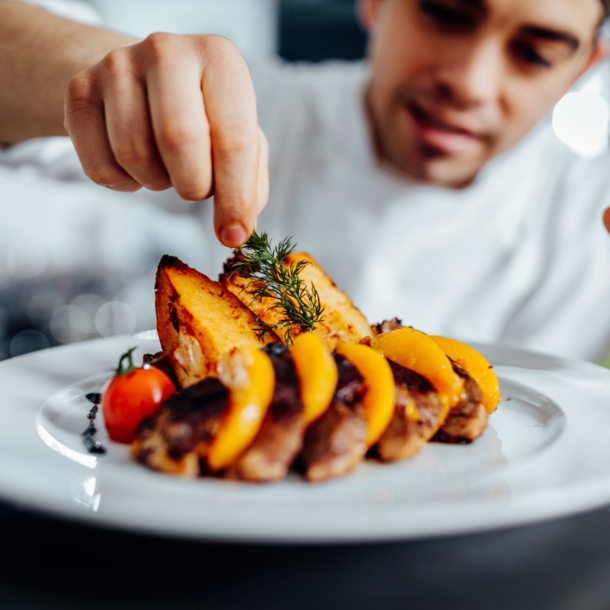 Ein junger Koch dekoriert ein angerichtetes Gourmet-Essen mit Kräutern