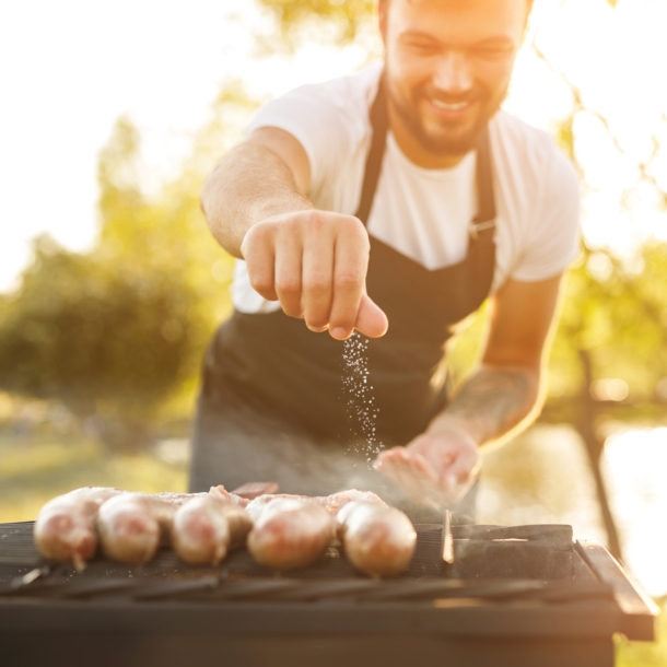 Mann streut Salz auf Würstchen die auf einem Grill liegen